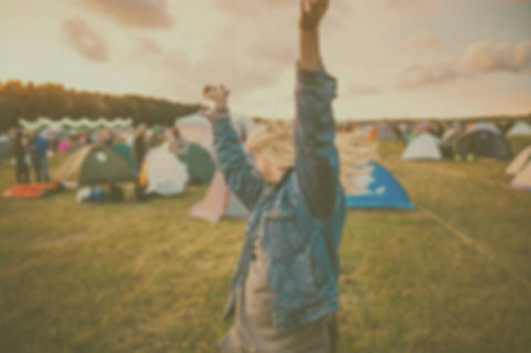 Das Bild zeigt eine junge Person in Feierstimmung vor einem Zeltplatz, wie man sie üblicherweise auf Festivals findet.